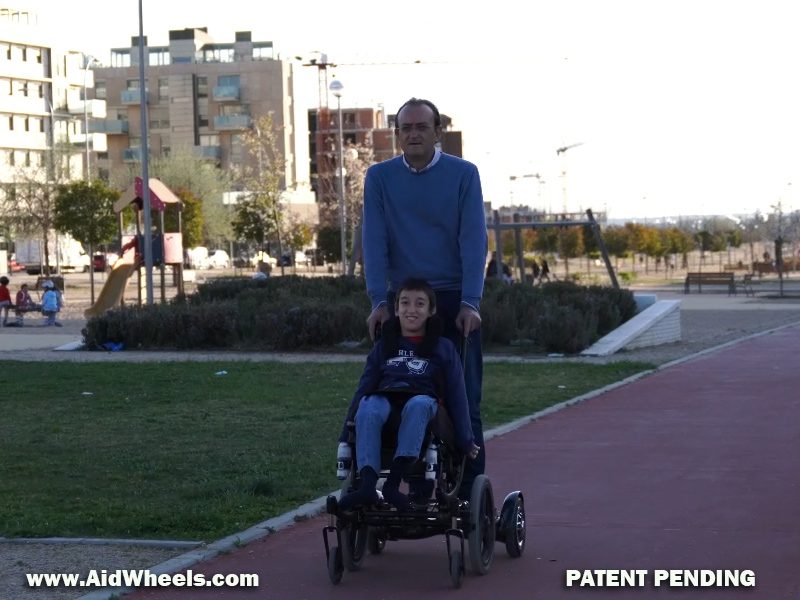 padre paseando hijo en silla de ruedas con un hoverboard